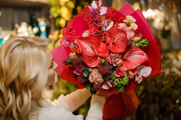 Жінка тримає червоний букет з різних квітів, прикрашений обгортковим папером . — стокове фото