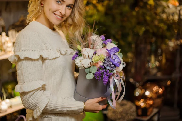 Encantador arreglo floral en colores blanco y púrpura en caja redonda en las manos de las mujeres — Foto de Stock