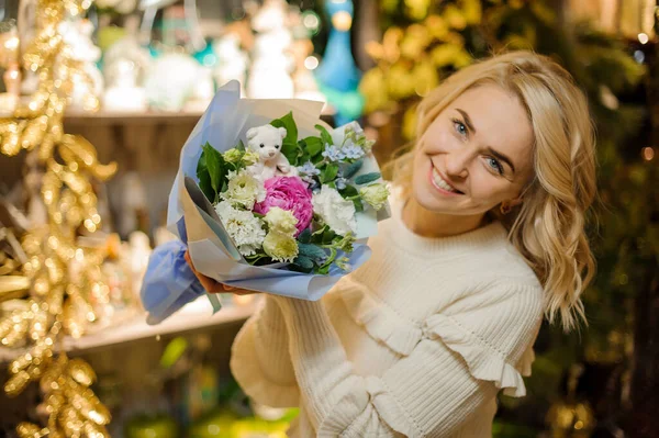 Mujer sonriente sosteniendo lindo ramo floral de flores frescas de primavera decoradas con osito de juguete. — Foto de Stock