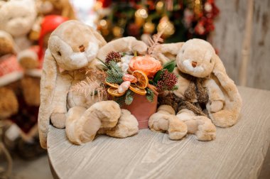 Yuvarlak kutuda sevimli çiçek aranjmanı ve yanında pelüş oyuncak tavşanlar.