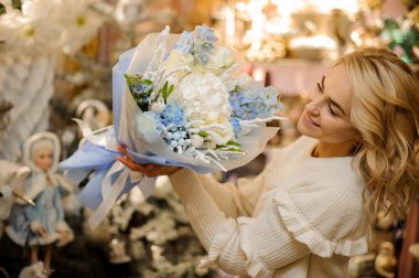 Farklı çiçeklerle süslenmiş narin bir çiçek buketi. Mutlu bir kadının ellerinde mavi kağıtla süslenmiş.