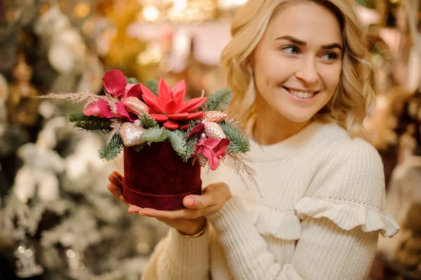 Φωτεινή δημιουργική διάταξη λουλουδιών διακοσμημένη με χρυσά στολίδια χριστουγεννιάτικων δέντρων στα χέρια της χαμογελαστής γυναίκας — Φωτογραφία Αρχείου
