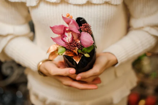 El primer plano de la flor rosada de la orquídea en la olla pequeña negra en las manos de la mujer. — Foto de Stock