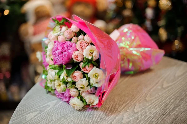 Close-up de delicado buquê de peônias e rosas envolto em papel rosa encontra-se na mesa — Fotografia de Stock