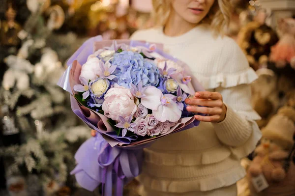 Impresionante ramo de flores envuelto en papel lila en las manos de la mujer — Foto de Stock