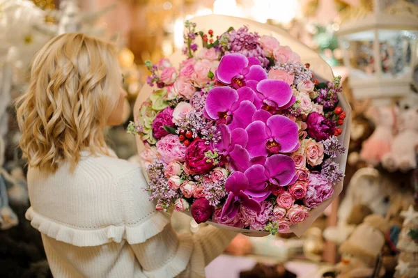 big chic bright bouquet of orchids and roses and peonies and lilacs on hands of blonde.