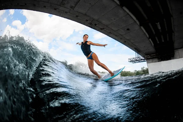 Молода мокра жінка в чорному плавальному жилеті майстерно балансує на річковій хвилі на дошці — стокове фото
