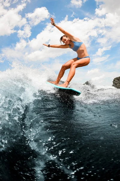 Attractive sports woman balancing on the wake board on high wave of motorboat