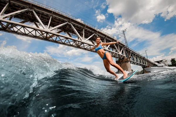 Femme sexy s'amuser et monter sur la planche sur la rivière sur fond de pont de la ville. — Photo