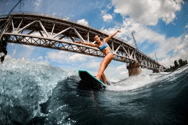 Femme debout sur la planche de réveil sur la vague haute sur le fond du pont de la ville. — Photo