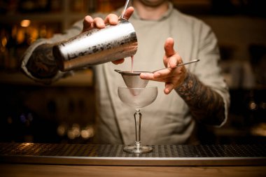 Erkek barmen, şarap kadehinin üzerinde elek tutar ve karıştırıcıdan kokteyl döker..