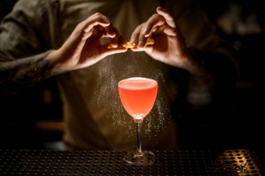 Barmen barmen limon kabuğunu tutuyor ve bardağa parlak bir kokteyl serpiyor..