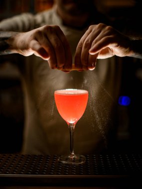 Barmenin limon kabuğu tutarken yakın plan görüntüsü ve bardağa ustaca serpiştirilmiş parlak bir kokteyl..