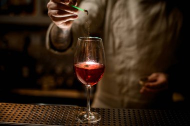 Barmen şarap bardağına kırmızı içecekle altın tozu ekler..