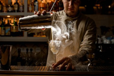 Erkek barmen buharı tüten içkisini buzlu şarap bardağına döker..