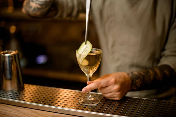 Vue du barman décore verre à cocktail avec tranche de concombre à l'aide de pince à épiler — Photo