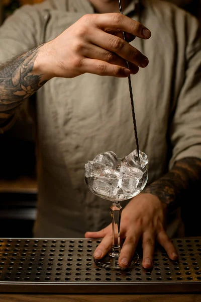 barman with long bar spoon stir the ice cubes in wine glass