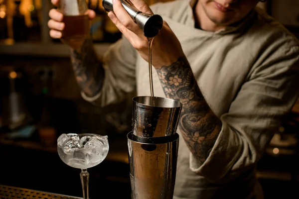 Cantinero hombre vierte bebida de metal jigger en agitador en barra mostrador — Foto de Stock
