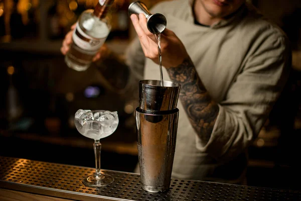 Camarero vierte cuidadosamente bebida de jigger de metal en agitador en barra de bar — Foto de Stock