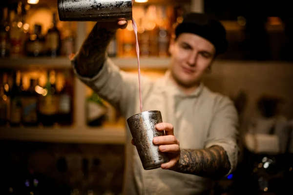 Joven barman sostiene vasos de coctelera en sus manos y vierte cóctel de ellos — Foto de Stock