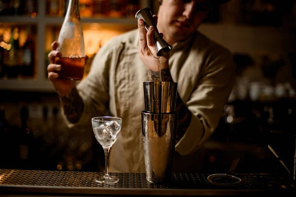 Vista en barman magistralmente vierte bebida de metal jigger en agitador en barra mostrador —  Fotos de Stock