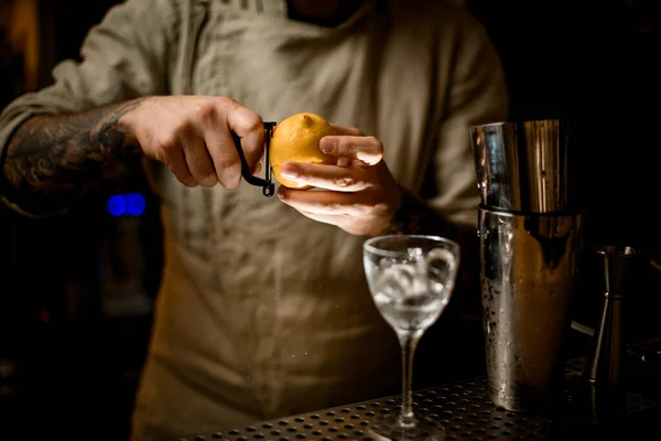 Bartender holds lemon in his hands and cuts the peel off with knife — Stock Photo, Image