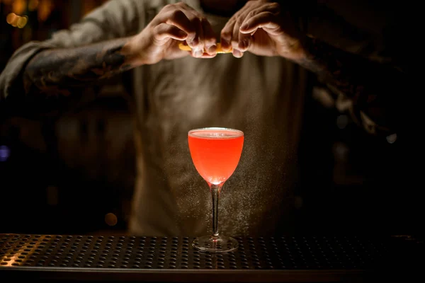 Man met citroenschil over glas met heldere cocktail en hagelslag erop. — Stockfoto