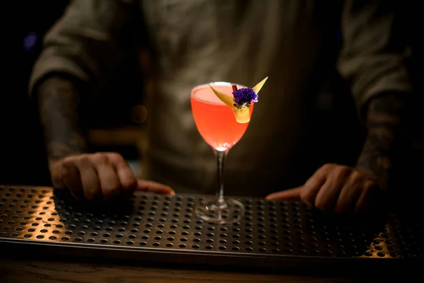 Widok na szkło z napojem, ozdobiony skórką cytryny i kwiatem, stoi na blacie baru. — Zdjęcie stockowe