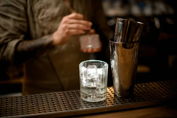 Прозоре старомодне скло з льодом і шейкером стоїть на барі з барменом на фоні — стокове фото