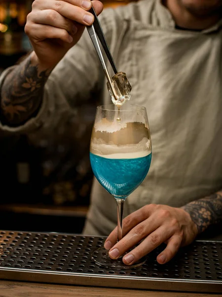 Man bartender exakt håller bit av is över ångande vin glas dekorerad med guld — Stockfoto