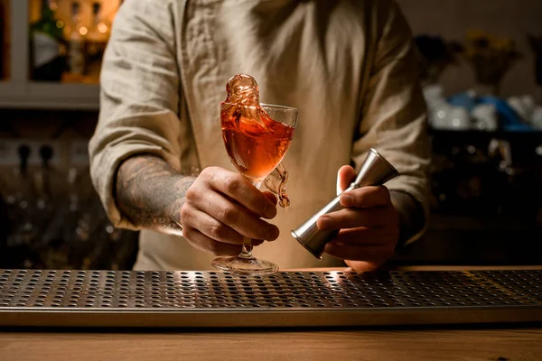 Camarero sostiene jigger y copa de cóctel con salpicadura de bebida alcohólica en sus manos — Foto de Stock