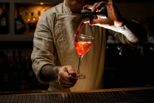 Αρσενικό μπάρμαν κατέχει με το χέρι ποτήρι κρασί με φωτεινό ποτό και προσθέτει υγρό από jigger — Φωτογραφία Αρχείου
