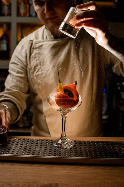 man at bar add ingredients to glass with small pumpkin and pepper inside