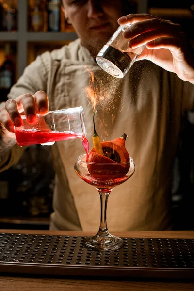 Barmann fügt gekonnt Zutaten zu Glas mit Gemüse drinnen hinzu und macht Feuer drüber — Stockfoto