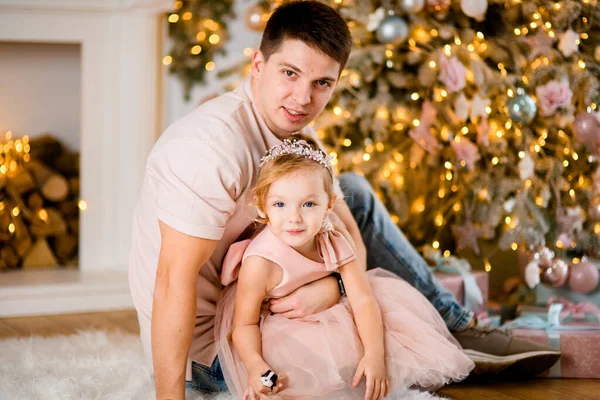 어린 아버지는 크리스마스 트리 근처에서 어린 딸과 함께 앉아 있다. — 스톡 사진