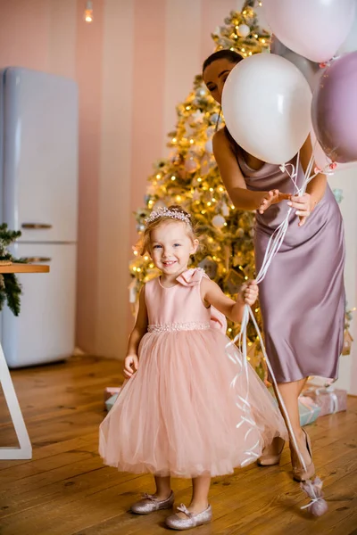 Pequeña chica divertida en rosa vestido de pie con globos en la mano — Foto de Stock