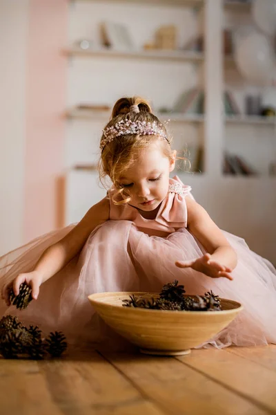 Linda menina em vestido rosa coloca cones de pinho na placa — Fotografia de Stock