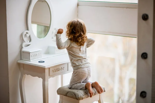 Vista trasera de la niña en pijama sentada delante del tocador con espejo — Foto de Stock