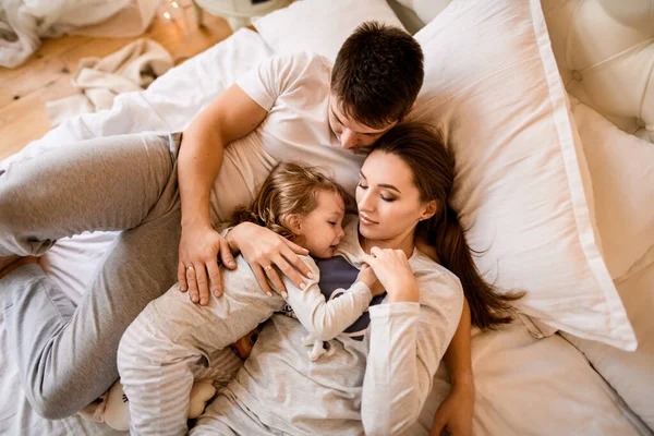 Vista di giovane coppia sposata con bambino piccolo in pigiama sdraiato sul letto — Foto Stock