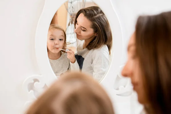 Reflejo en espejo de mujer y niña que se pinta los labios con brillo labial. — Foto de Stock