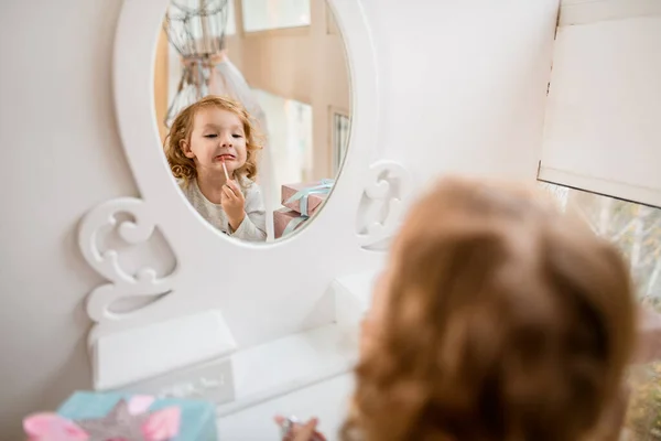 입술을 립글로스로 물감는 사랑 스러운 소녀의 모습을 반영 한 거울. — 스톡 사진