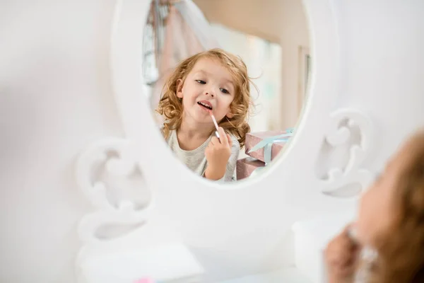 Reflejo en espejo de niña que se pinta los labios con brillo labial. — Foto de Stock