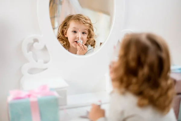 Refleksi di cermin gadis kecil memegang sikat lip gloss di depannya — Stok Foto