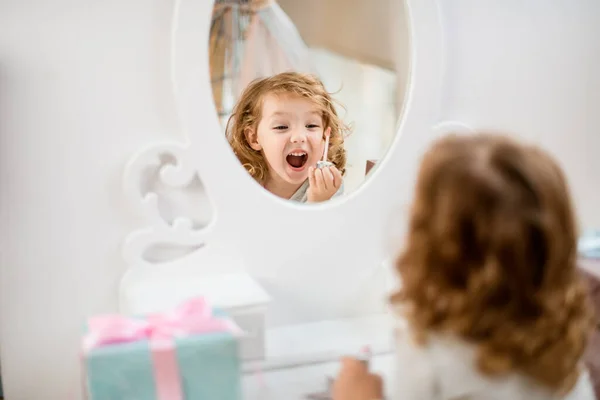 Reflexión en el espejo de una niña gritando sosteniendo un cepillo de brillo de labios delante de ella — Foto de Stock
