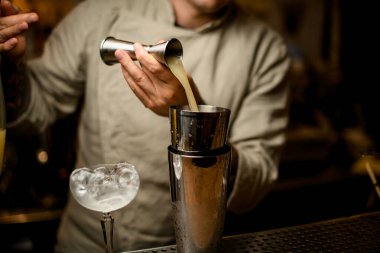 Barmen dikkatli bir şekilde barın tezgahına metal jigger 'dan karıştırıcıya su doldurur.