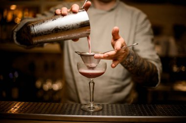 Barmen şarap kadehinin üzerine elek tutar ve karıştırıcıdan kokteyl döker..