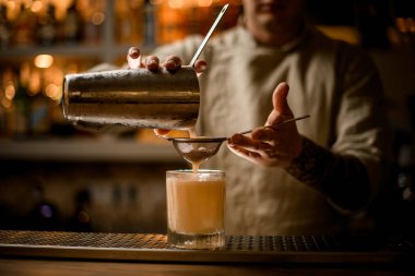 Erkek barmen eski moda bardakları süzer ve karıştırıcıdan kokteyl döker..