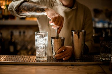 Erkek barmen karıştırıcıyı kullanarak karıştırıcı bardakta kokteyl hazırlar.