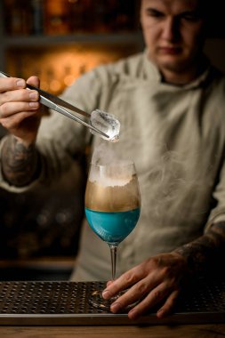 Adam altın madalyayla süslenmiş şarap kadehinin üzerinde buz tutuyor.