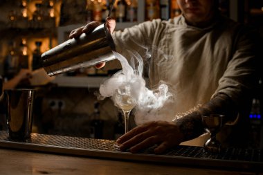 Barmen, bardaktan şarap bardağına dumanı dolduruyor.